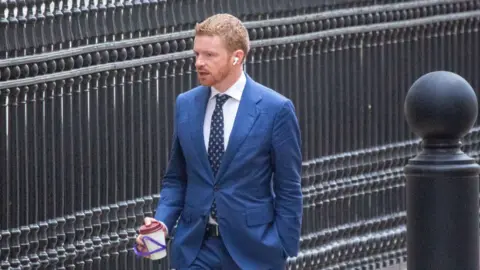 Alamy Morgan McSweeney walking up Downing Street wearing a blue suit and holding a coffee cup and wearing earpods