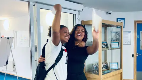 Two girls jump in the air with their GCSE results in-hand
