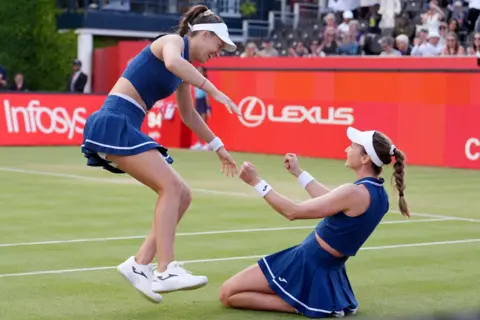 PA Media Tereza Mihalikova and Olivia Nicholls celebrating their women's doubles win at Queen's. Nicholls, who is on the right, is kneeling on the floor with her fists clenched and Mihalikova is standing up reaching over to hug her.