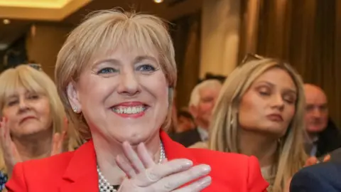 Getty Heather Humphreys, a woman with short blonde hair, wearing a red suit, earrings and a pearl necklace applauds during the Fine Gael convention at the Sheraton Hotel in Athlone, central Ireland on March 24, 2024