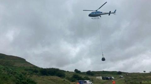 A helicopter flies above Roseberry Topping carrying a one-tonne bag of paving stones on a wire.
