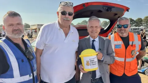 Phillip Norton/BBC. Personal de GBC Security fotografiado con Peter Levy. Están de pie juntos frente a un Ford Fiesta rojo.