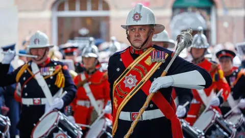 Getty Images Members of Devon and Somerset Fire and Rescue Service are marching in uniform and white hard hats, some playing the drums.