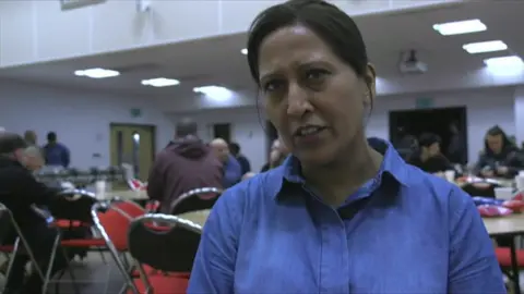 A woman with her hair tied back and wearing a blue shirt looks at the camera