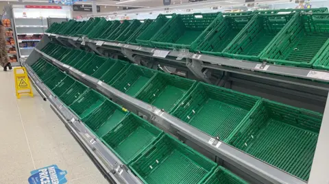 Green plastic boxes normally filled with fruit and vegetables lie empty inside the supermarket.