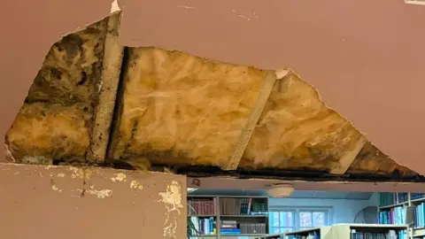 A large hole in a pink ceiling of a bookshop has exposed roof beams and insulation.