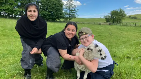 BBC/Olivia Richwald Three children with a lamb
