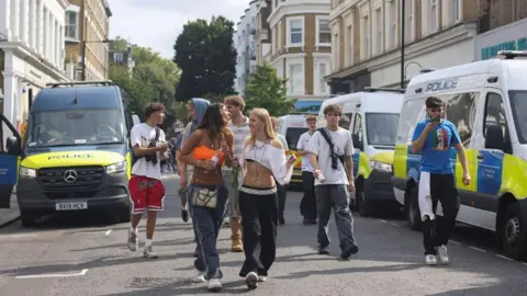 Reuters Image of a group of teens walking down the road in between two police vans at Notting Hill Carnival in 2024