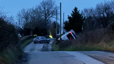 A bus is in the ditch and a silver police car is parked on the road.