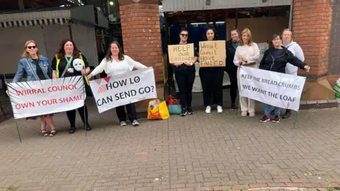 BBC The parents standing outside Birkenhead Market holding signs asking for help for their children