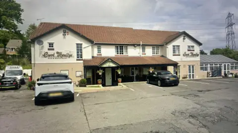 Google The outside of a hotel with two cars parked out front.