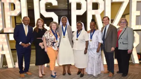 ACCI A row of men and women are smiling at the camera. Behind there are large white letters that read Opus Prize