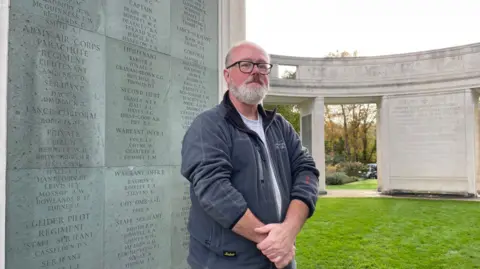 BBC/ClareCowan Senior gardener Bob Thomson wearing gardening clothes and standing in front of graves at Brookwood Military Cemetery.