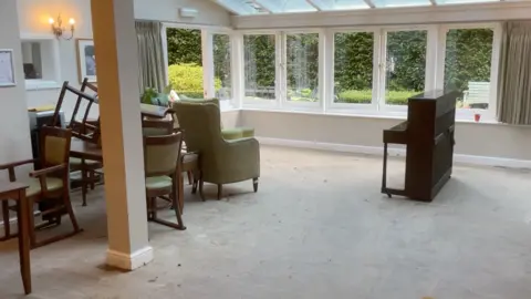 The ground floor of the care home with a piano, chairs and windows