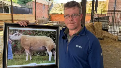 Farmer David Thornley holds a framed picture of one of his prize-winning rams