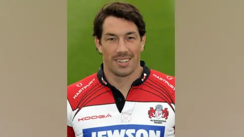 Getty Images Tom Voyce wearing a red and white Gloucester Rugby shirt. He had side-parted brown hair and is smiling at the camera.