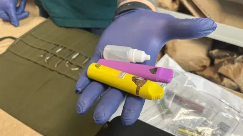 BBC Illegal vapes and an illegal vape refill in the hand of a police officer
