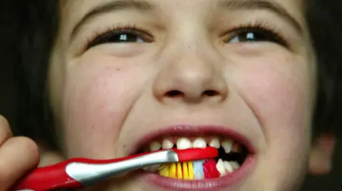 PA Media A child brushes their teeth with a colourful toothbrush.