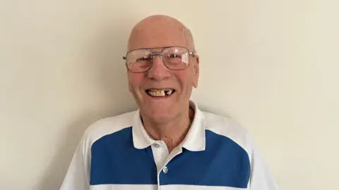 Ben Parker/BBC Reginald Wright wearing a blue and white shirt polo shirt, smiling at the camera.