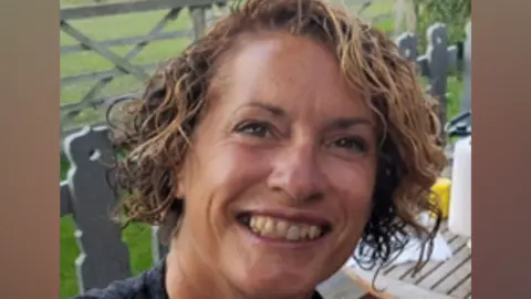 Bedfordshire Police Marian Bicknell, with short curly dark hair, smiling, looking at the camera, outside, by a table.