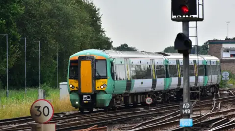 Southern A green and white train moving on railway tracks. There are green trees and grass to the side. 