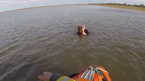 Man reaching out to another man holding a dog in the sea