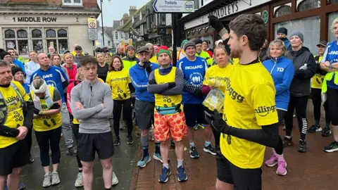 BBC/Juliette Parkin James Cooper surrounded by other runners, all wearing running gear, in East Grinstead.