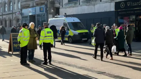 People and police walking in Cornmarket Street in Oxford, with a police van behind.