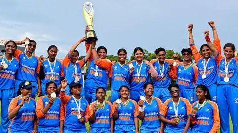 Getty Images India's players, sorting their blue and saffron jerseys, pose with their medals and the trophy after winning against Nepal at the Blind Women's Twenty20 World Cup 2025 final match in Colombo on 23 November 2025