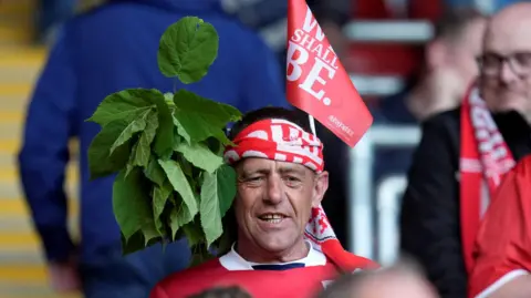 PA A Middlesbrough fan ahead of the Sky Bet Championship play off semi-final at St Mary's Stadium, Southampton. He has tied a red and white scarf around his head. On one side, he has tucked in a bunch of leaves. On the other, is a small read flag.