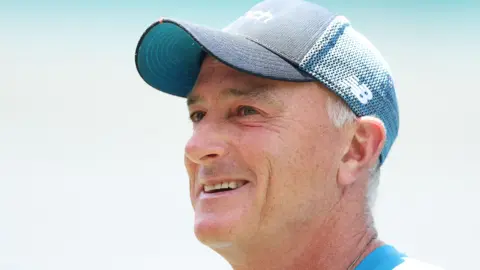 Getty Images England assistant coach Graham Thorpe talks to media during an England nets session at Sydney Cricket Ground on January 04, 2022 in Sydney, Australia. He is smiling and wearing a dark & light blue cap. He is looking up and to the left of the screen