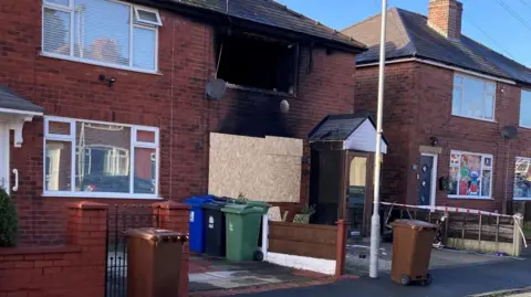 Burnt-out house after the fire was put out. It is boarded up and blackened. 