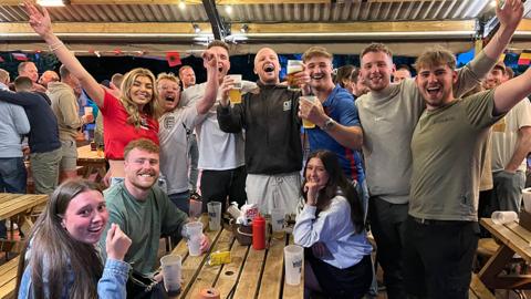 Dozens of jubilant England fans celebrate at the White Horse pub after the team's win over the Netherlands in the Euro 2024 semi-final, many standing with their arms aloft