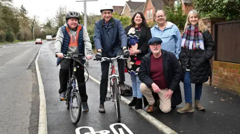 Reading Borough Council Two male cyclists on bikes posing in a cycle lane. They are standing with four other people, who are on the pavement.