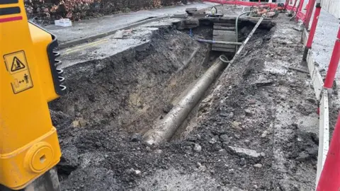 An exposed water man in an excavated hole in the road.