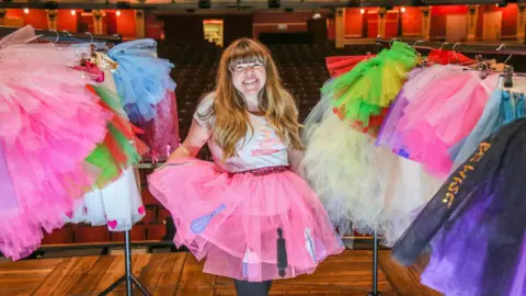 Flamingo Chicks Briony May Williams wearing a tutu on stage at the Bristol Hippodrome, surrounded by clothing rails of other tutus