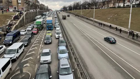 Four lanes of traffic are completely filled by a traffic jam in one direction, while the other direction is virtually empty