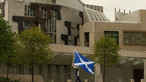 Getty Images A man holds a Saltire flag outside the Scottish Parliament