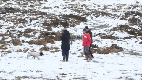 PA People walking a dog on a snowy Dartmoor