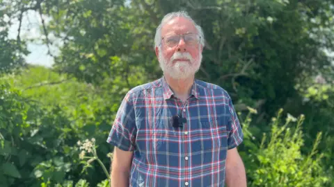 Man in chequered shirt stood next to shrubbery