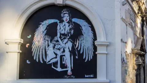 Black and white painting of Amy Winehouse with angel wings on the wall of Koko