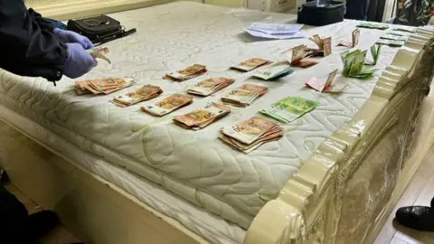 Europol A police officer counts out euro notes on a bedspread. There are stacks and stacks of cash, with 100, 50 and 200 euro values on them