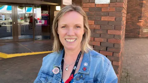 Councillor Sharon Harvey is wearing a blue denim jacket, standing outside Redditch Library. 