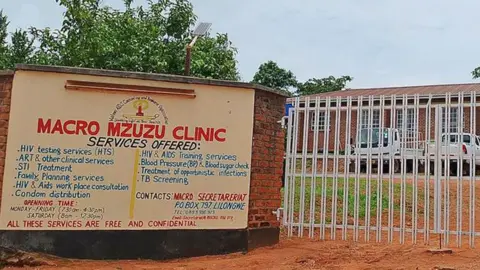 Sebuah tanda oleh gerbang tertutup klinik makro Mzuzu di Malawi yang merinci layanan HIV gratis yang ditawarkan.