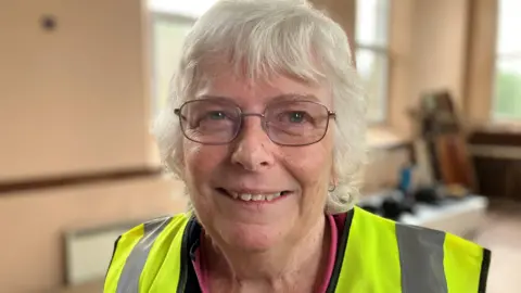 Sheila Trethewey in a hi-visibility jacket. She is an older woman with short grey hair and glasses.