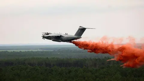 AFP via Getty Images Plane drops red fire retardant over woodland. 