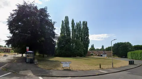 A generic photo featuring the road called Gamesfield Green at the bottom of the image, an area of grass behind the street sign and trees behind the grass on the photo.