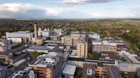 BBC Aerial view of Addenbrooke's Hospital and other buildings in the Cambridge biomedical campus. In the distance are houses and fields.