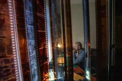 Fritz Pinnow Fabriccio Díaz works on his computer in the room of his apartment that has been converted into an office. In the foreground, rolls of film are hanging out to dry. 