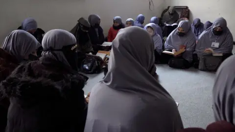 Women, whose faces are covered, it on the floor studying